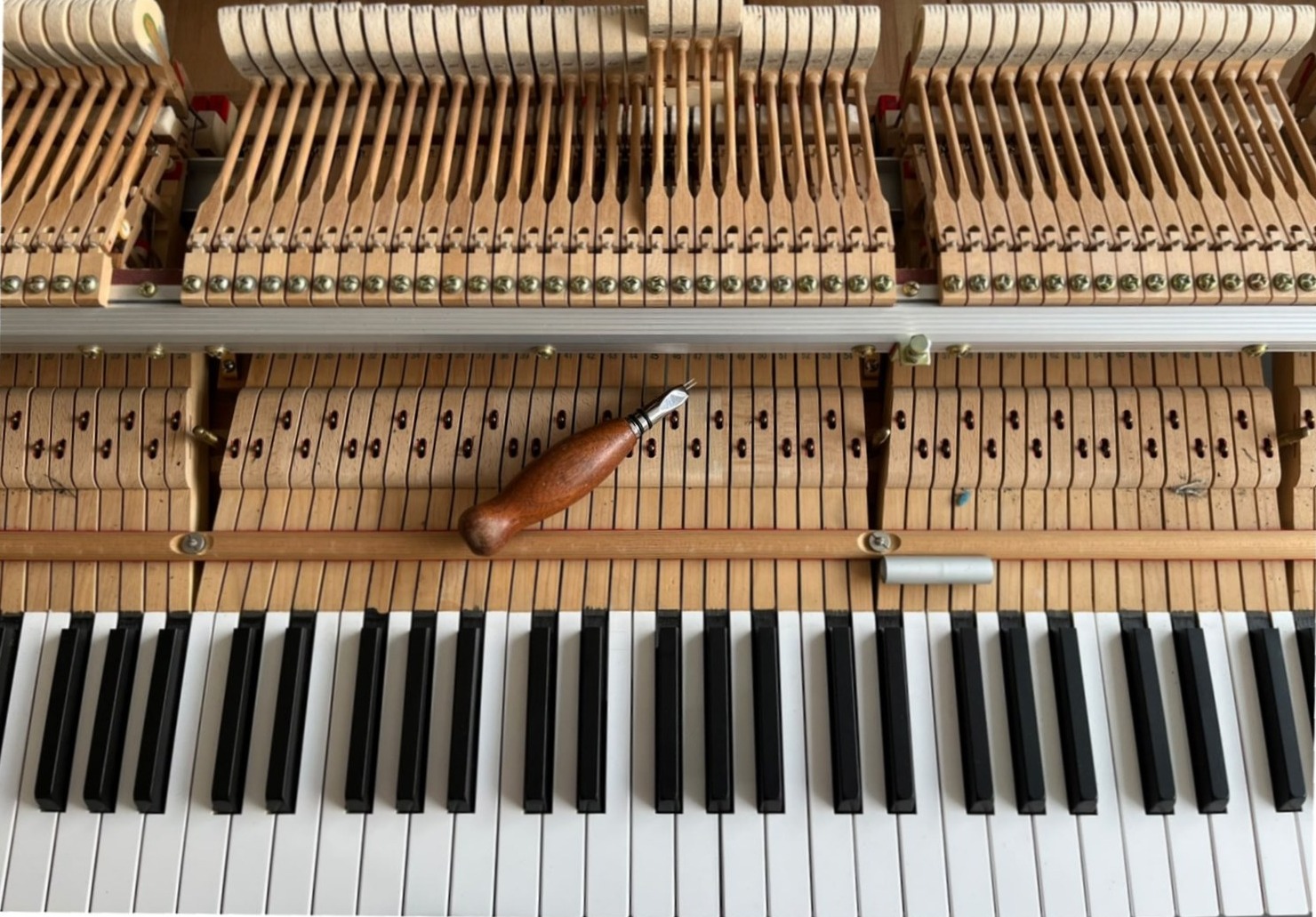 Clavier et mécanique d'un piano droit ouverts, un outil de réglage posé